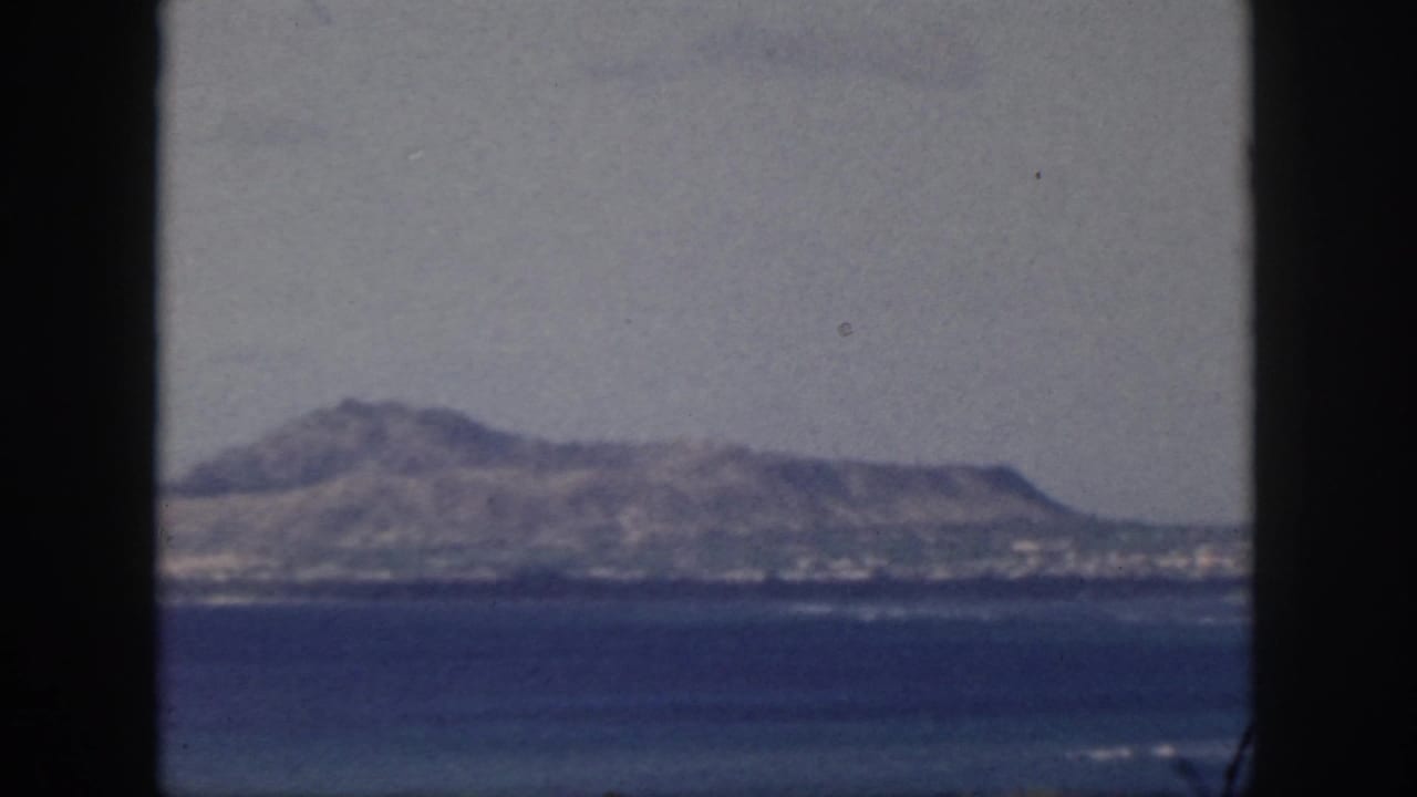 1959 Oahu coastal view with blue ocean, hazy sky, and rugged ridge framed by dark vertical bars.