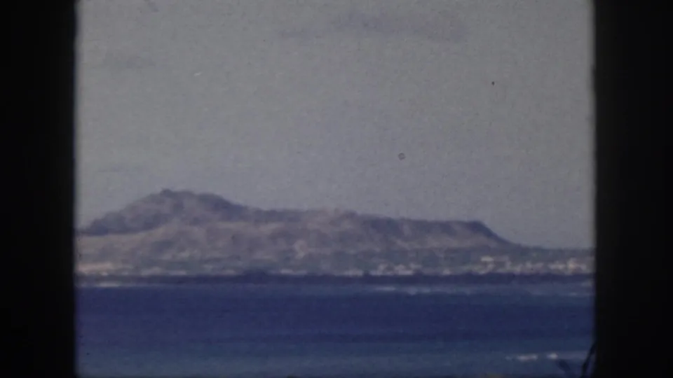 1959 Oahu coastal view with blue ocean, hazy sky, and rugged ridge framed by dark vertical bars.