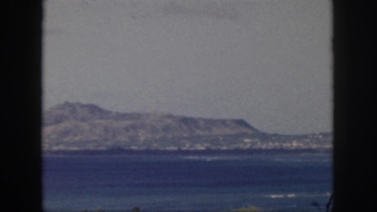 Oahu coastline in 1959, showing ocean foreground, distant arid hills, and dark frame edges.
