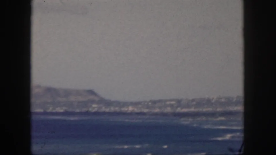 1959 Oahu shoreline and ocean seen past a dark central frame, with hazy hills in the distance.
