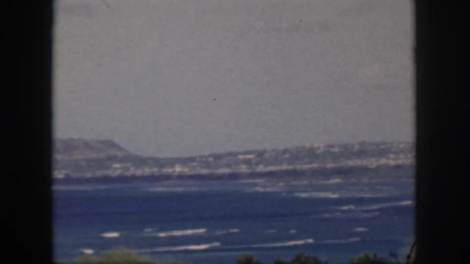 1959 Oahu coastal view with blue water, white surf lines, distant hills, and a dark foreground frame.