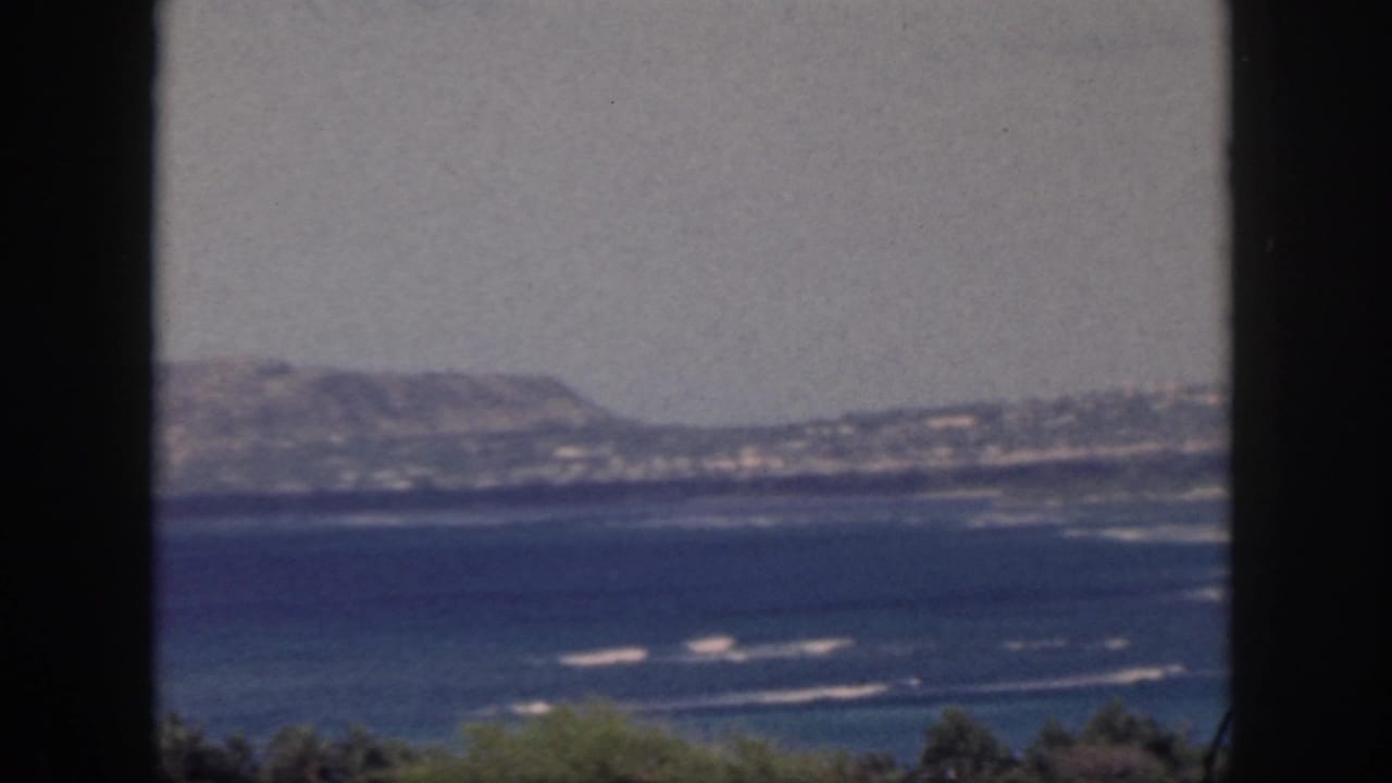 Oahu shoreline and low mountains appear beyond blue water, partially divided by a dark foreground frame.