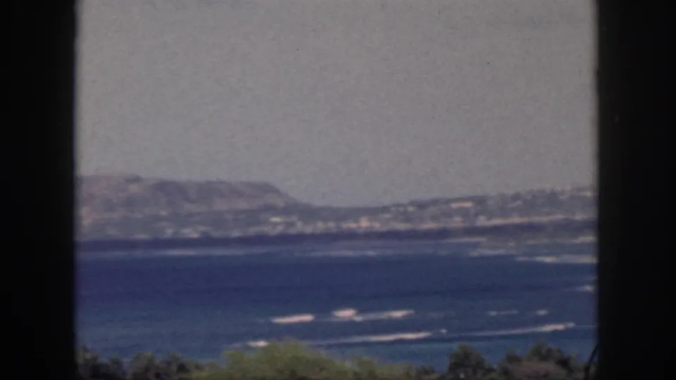 Oahu shoreline and low mountains appear beyond blue water, partially divided by a dark foreground frame.