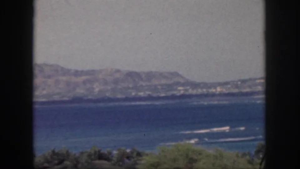 1959 Oahu coastal landscape with blue water, white surf, distant mountains, and dark vertical foreground edges.