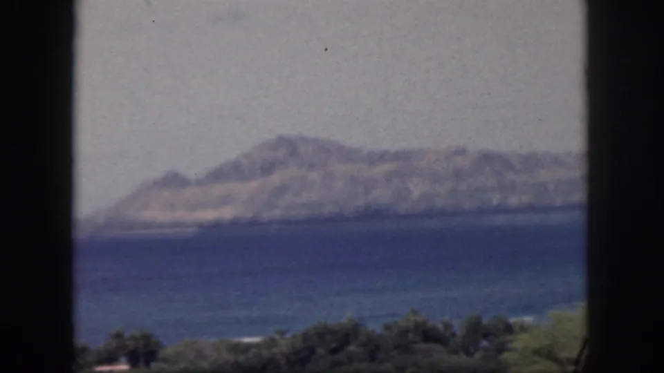 Soft 8mm 1959 Oahu landscape showing blue ocean, blurred distant hills, and dark foreground window framing.