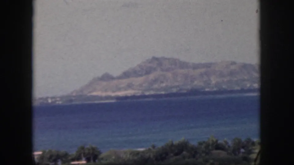 1959 Oahu 8mm frame of distant coastal hills and blue ocean, with foreground vegetation and dark window borders.