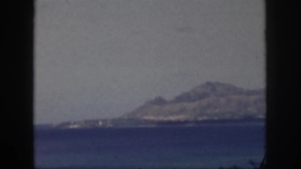 1959 Oahu 8mm frame with a softened distant mountain and shoreline across water, viewed through dark window framing.