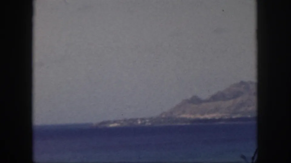 1959 Oahu home-movie view of a hazy mountain ridge across a calm bay, seen through dark vertical frame edges.