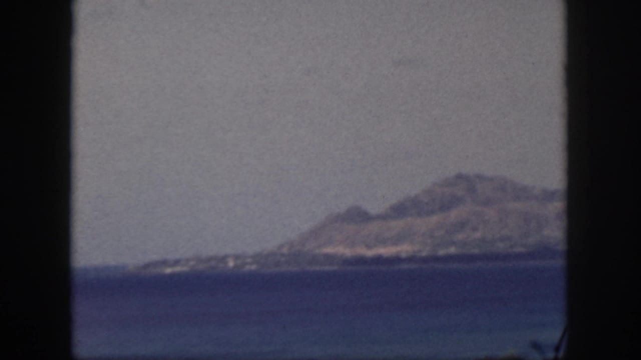 Mountain and shoreline across calm blue water with dark vertical borders in the foreground.