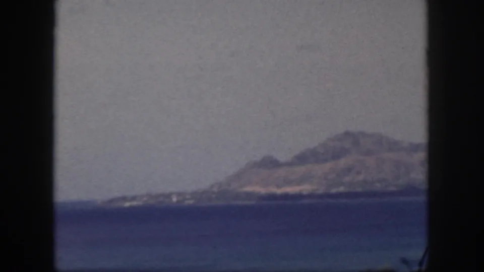Hazy 1959 Oahu coastal view with a mountain ridge, shoreline, and deep blue bay framed by dark vertical edges.