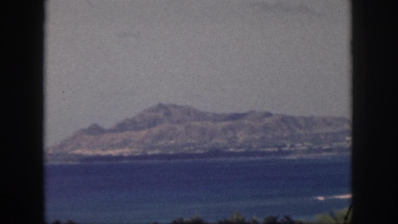 1959 Oahu 8mm frame showing a distant rugged ridge beyond blue water under a hazy sky.