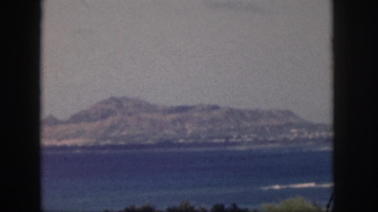 1959 Oahu home-movie view of a mountain range across water, with soft focus and dark gate edges.