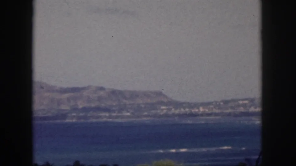 1959 Oahu coastal landscape showing low mountains and shoreline across blue water in soft 8mm color.