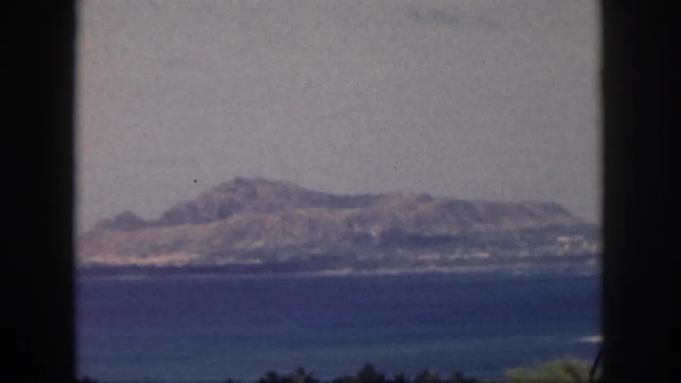 1959 Oahu coastal view with blue water, distant shoreline, and mountain range seen through a dark window frame.