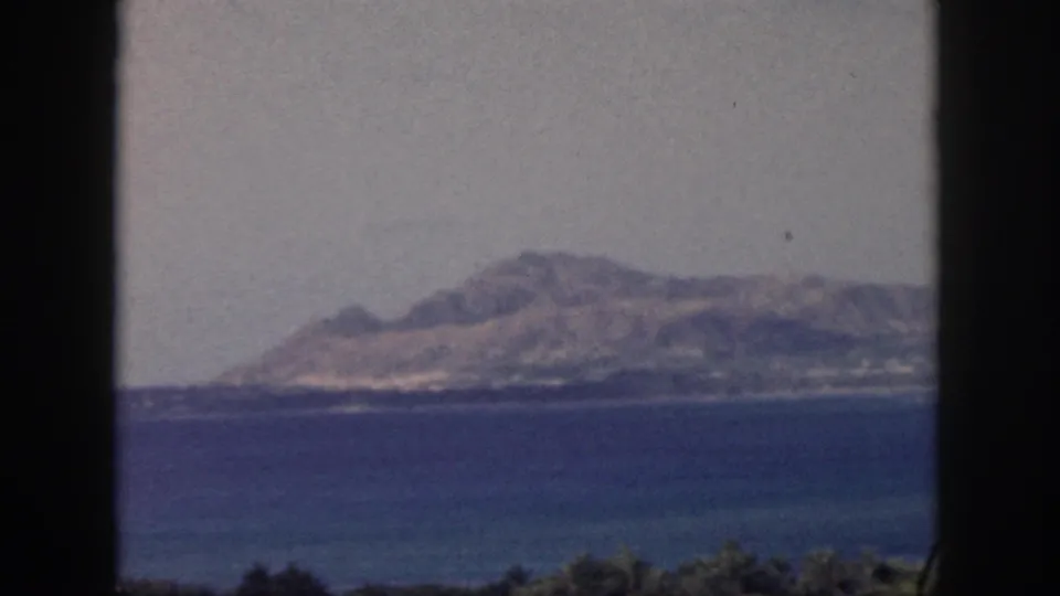 1959 Oahu 8mm frame with a softened view of a mountain range beyond the bay and dark foreground framing from a sheltered position.