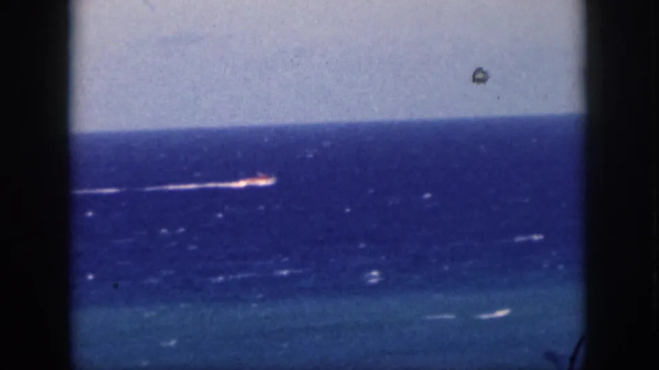 1959 Oahu home-movie frame with a small red-and-white boat crossing blue ocean and trailing a white wake.