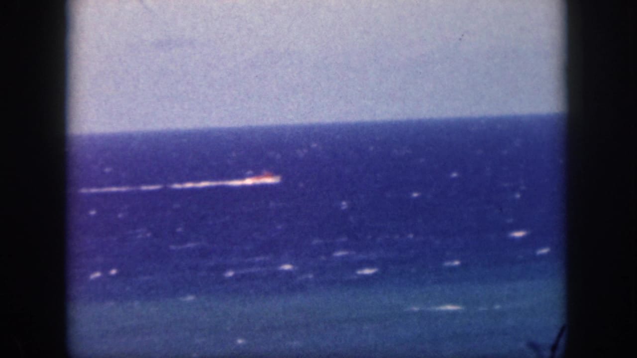 1959 Oahu home-movie frame showing a distant motorboat moving across blue ocean water with a white wake and visible film borders.