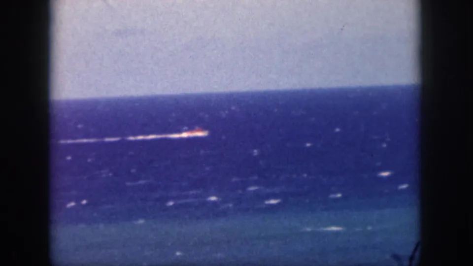 1959 Oahu home-movie frame showing a distant motorboat moving across blue ocean water with a white wake and visible film borders.