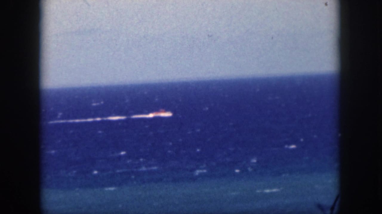 1959 Oahu 8mm frame with a small motorboat farther across the ocean, its white wake visible beneath a pale horizon.