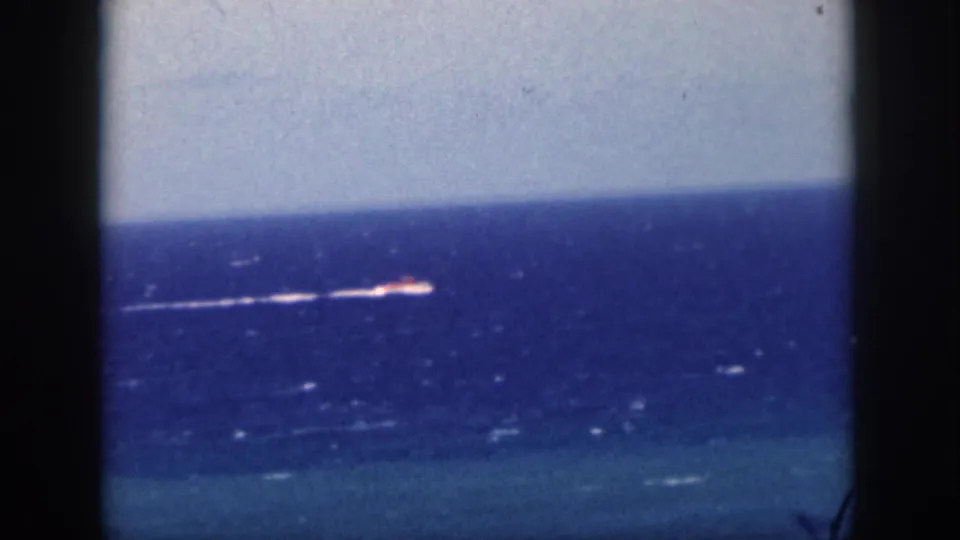 1959 Oahu 8mm frame with a small motorboat farther across the ocean, its white wake visible beneath a pale horizon.