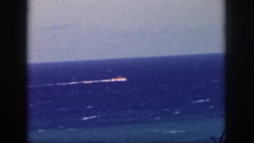 1959 Oahu home-movie frame showing the motorboat wake stretched across choppy blue water with soft focus and film grain.