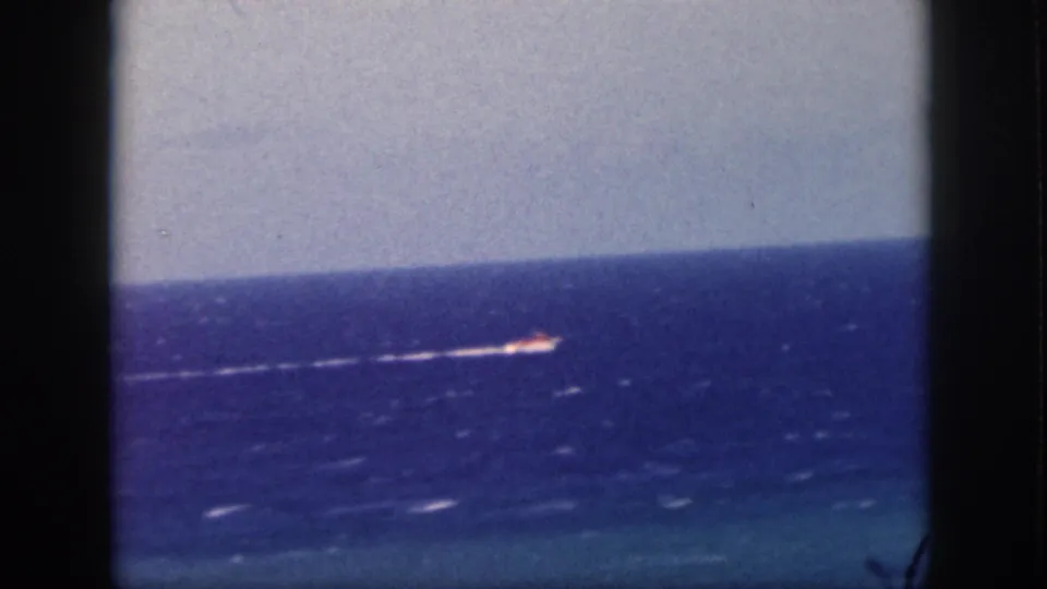 1959 Oahu 8mm frame showing a distant small boat near the horizon, trailing a white wake across the blue sea.