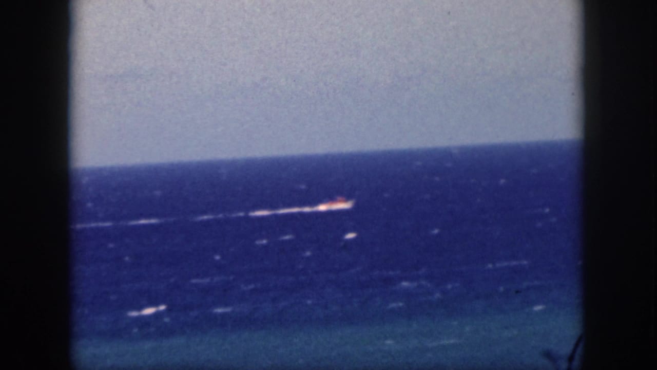 1959 Oahu home-movie frame showing a distant vessel crossing the Pacific, viewed through a dark cruise-window frame.