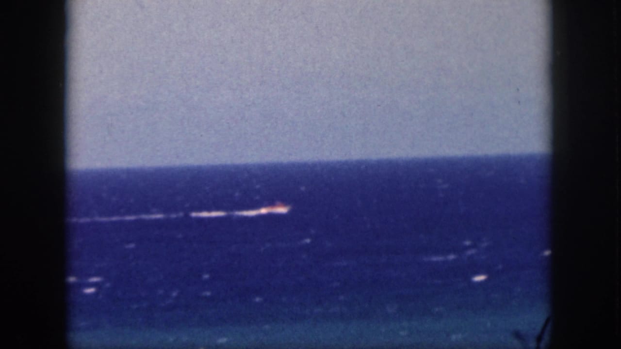Small bright vessel and white wake on the horizon beyond a window frame.