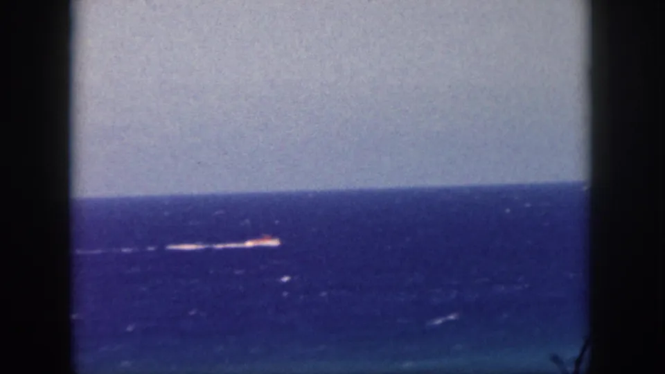 Vintage 8mm view from Oahu metadata showing a distant vessel on the Pacific, softened by grain and faded color.