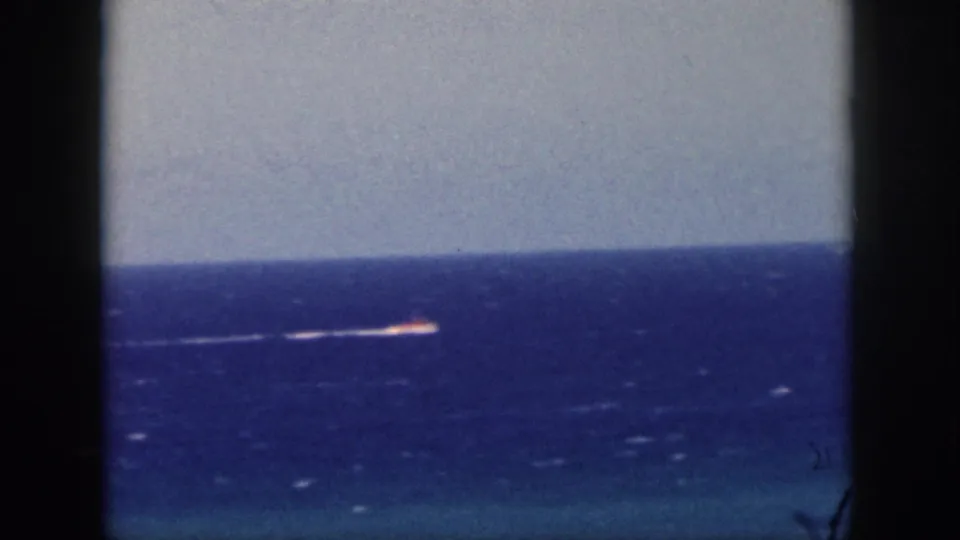 End frame of a 1959 Oahu travel shot, with a small vessel and wake visible through a dark window frame.