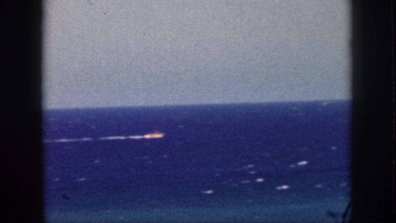 1959 Oahu 8mm frame showing a small distant boat moving across a blue ocean horizon beneath a pale sky.
