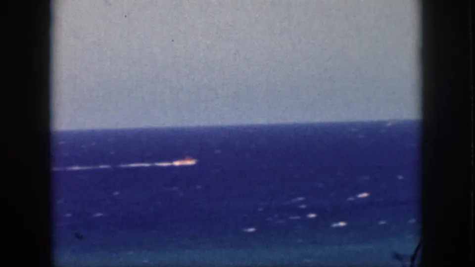 1959 Oahu 8mm frame showing a small distant boat moving across a blue ocean horizon beneath a pale sky.