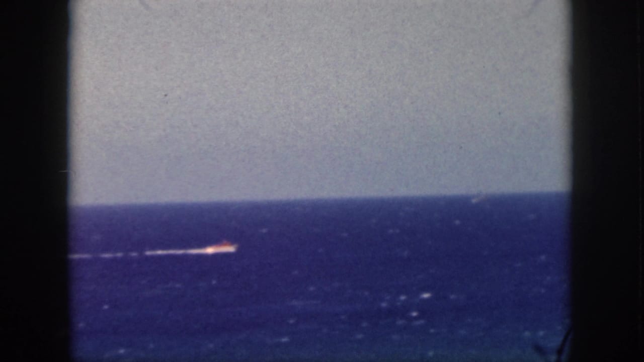 Small distant vessel and white wake on a blue sea horizon.