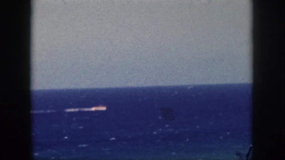 1959 Oahu 8mm frame with a distant vessel wake crossing the blue sea, framed by dark gate edges.