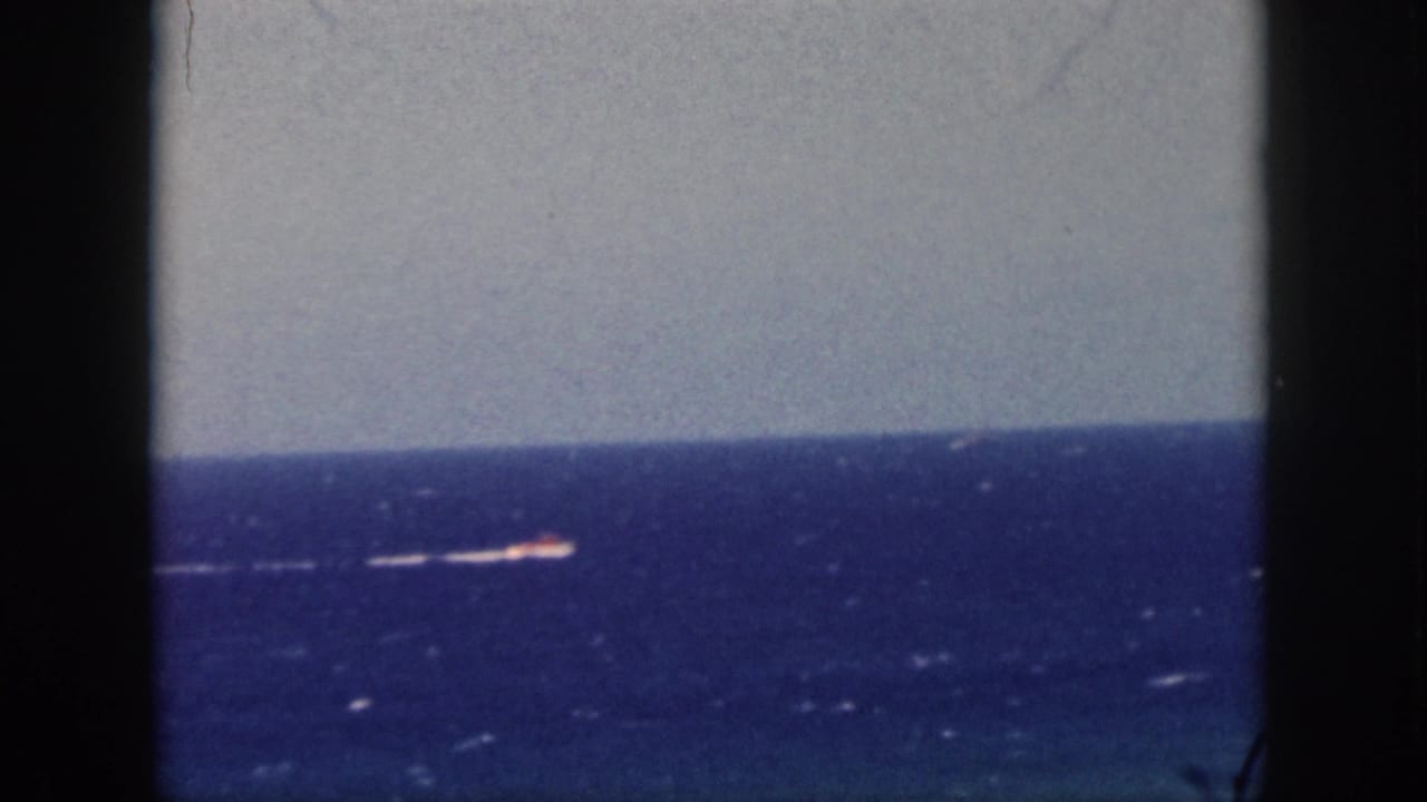 1959 Oahu home-movie frame showing a small motorboat and white wake on deep blue ocean, seen through dark framing edges.