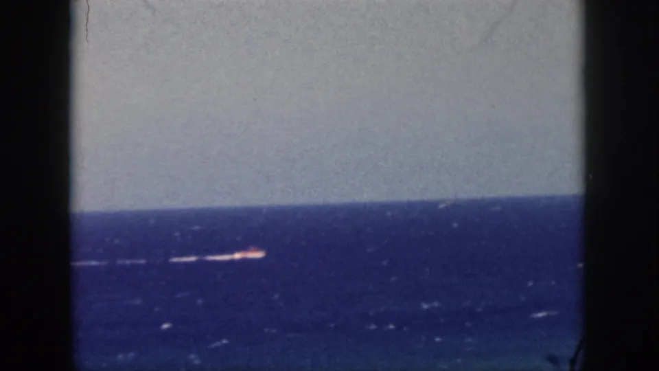 1959 Oahu home-movie frame showing a small motorboat and white wake on deep blue ocean, seen through dark framing edges.