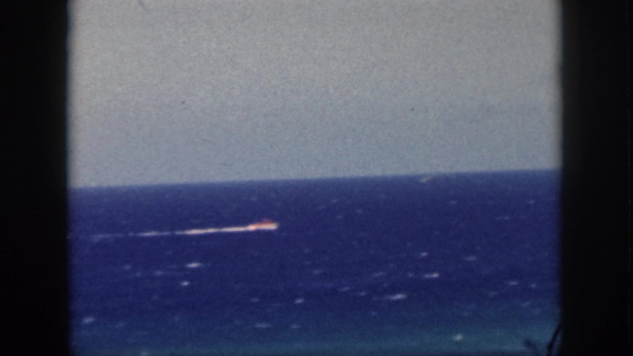 1959 Oahu 8mm frame with a distant motorboat moving across blue Pacific water, with dark vertical framing at the sides.