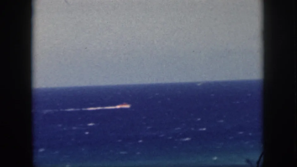 1959 Oahu 8mm frame with a distant motorboat moving across blue Pacific water, with dark vertical framing at the sides.