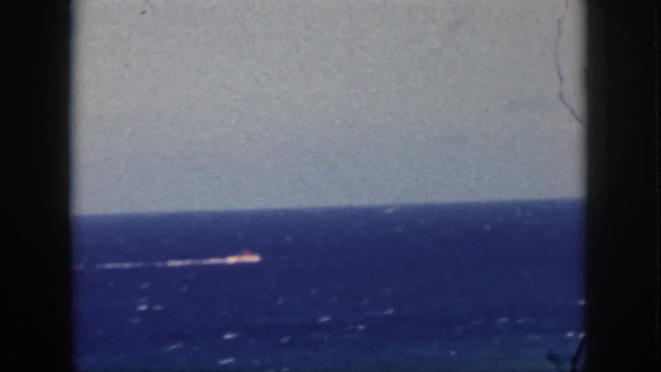 1959 Oahu vacation footage frame showing a small boat near the horizon on blue ocean, viewed through dark frame edges.