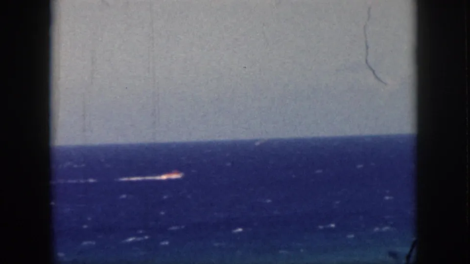 1959 Oahu home-movie frame of a distant motorboat on open ocean, with white wake and visible film wear.