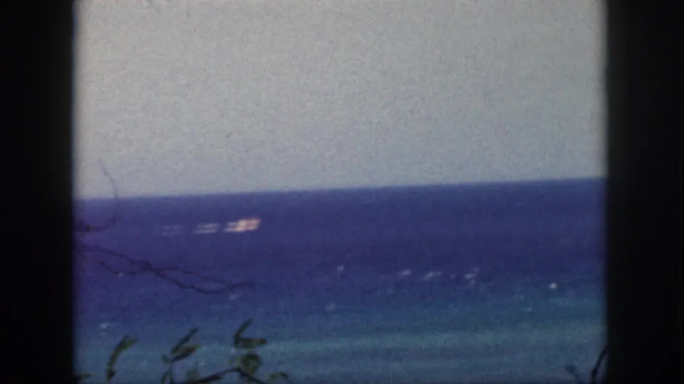 Final 1959 Oahu frame showing the ocean through window mullions, with a small distant boat-like form on the water.