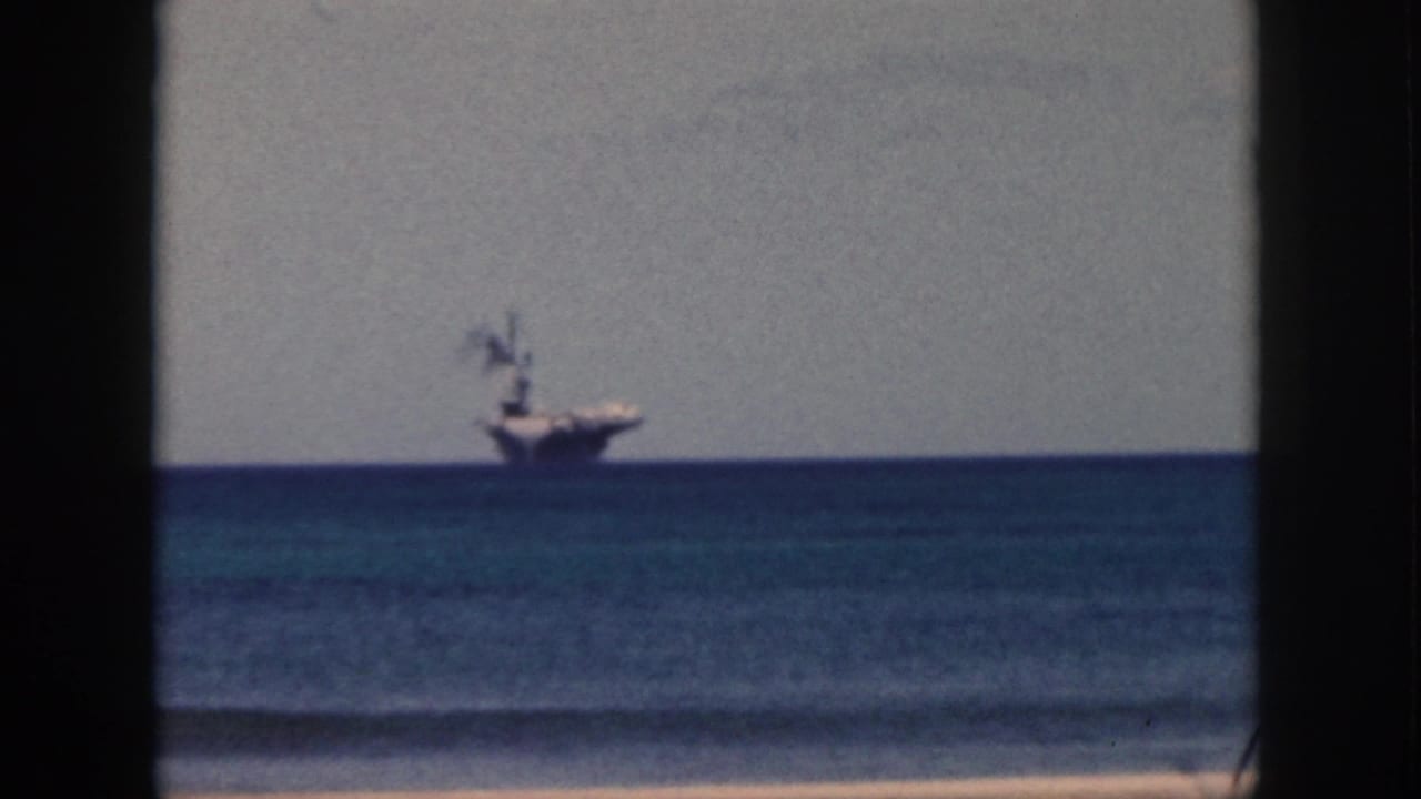 Distant aircraft carrier on the ocean horizon viewed through dark vertical framing.