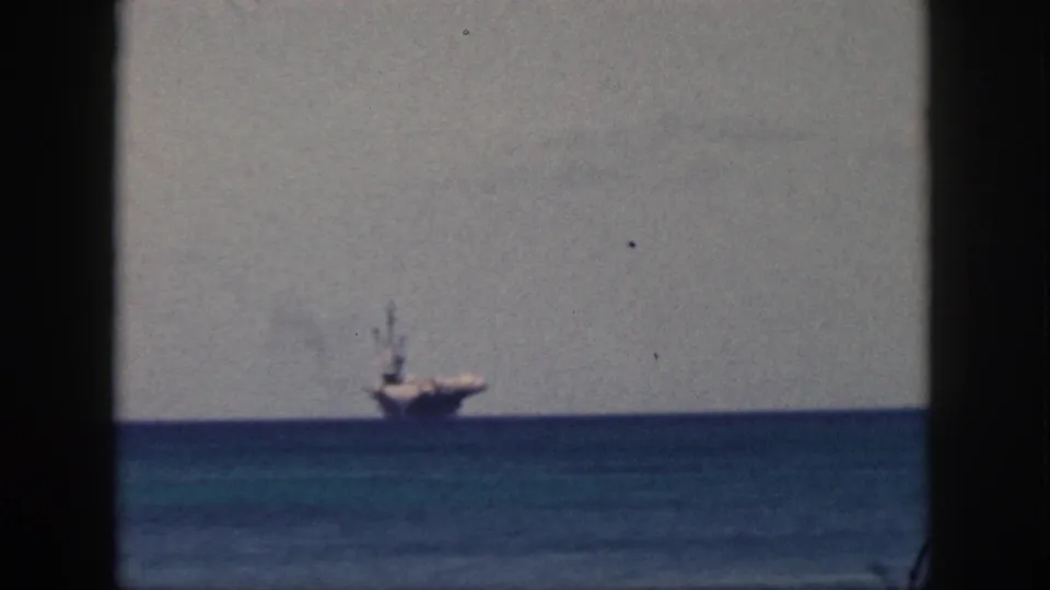 Final 1959 Oahu frame showing the distant carrier at sea, smoke above its stack, and a dark vertical foreground border.
