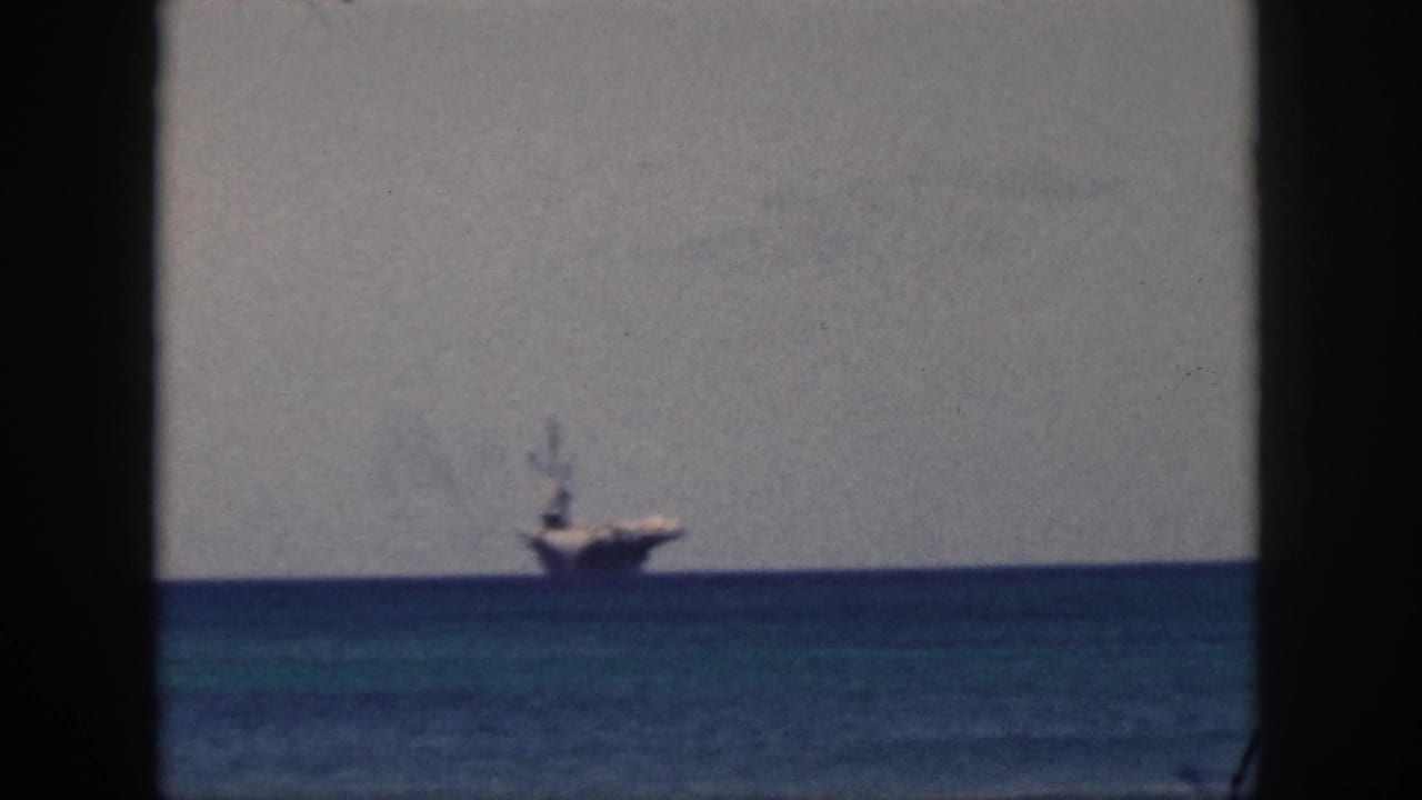 1959 Oahu home-movie frame showing a distant naval-looking ship on the blue ocean horizon through a dark window opening.