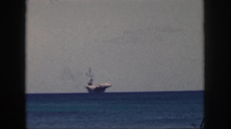 1959 Oahu home-movie frame showing a distant naval-looking ship on the blue ocean horizon through a dark window opening.