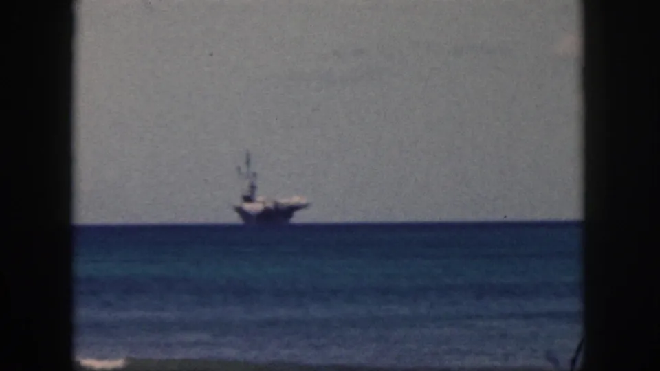 1959 Oahu 8mm frame with a distant ship offshore, dark window or balcony edge, blue water bands, and hazy sky.