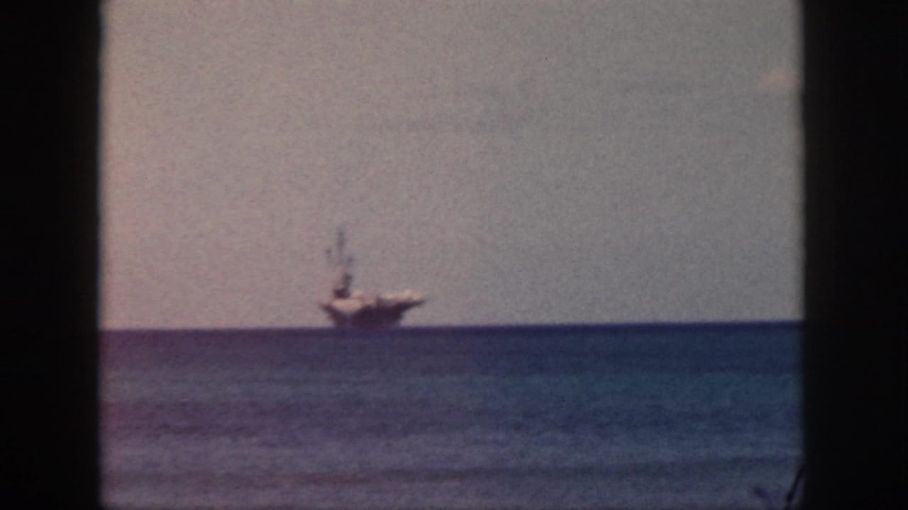 Aircraft carrier on the horizon over calm blue water with heavy dark frame edges.
