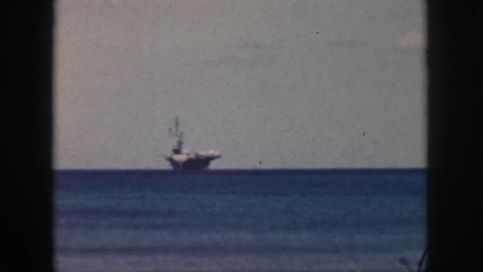 Oahu coastal view with a distant aircraft carrier beyond calm water, recorded on 8mm film in 1959.