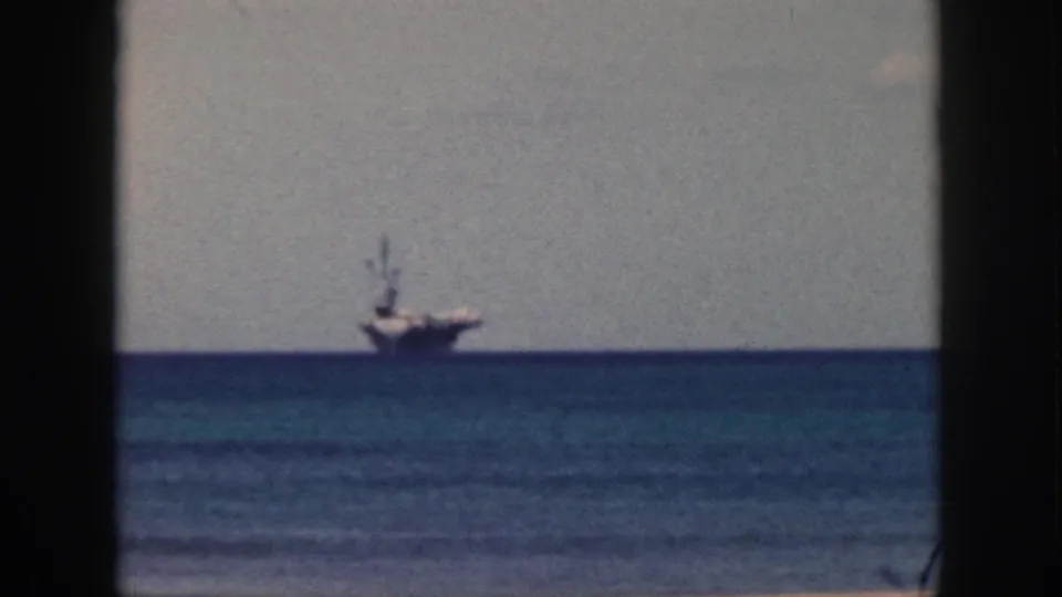 Final 1959 Oahu frame with the aircraft carrier still offshore, seen through soft grain and dark 8mm borders.