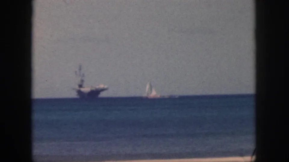 1959 Oahu 8mm frame with a large distant naval-looking ship and a small sailboat to the right on the ocean horizon.